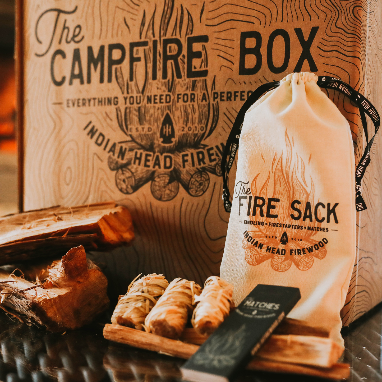 Campfire box with firewood, matches, and fire sack against a wooden background